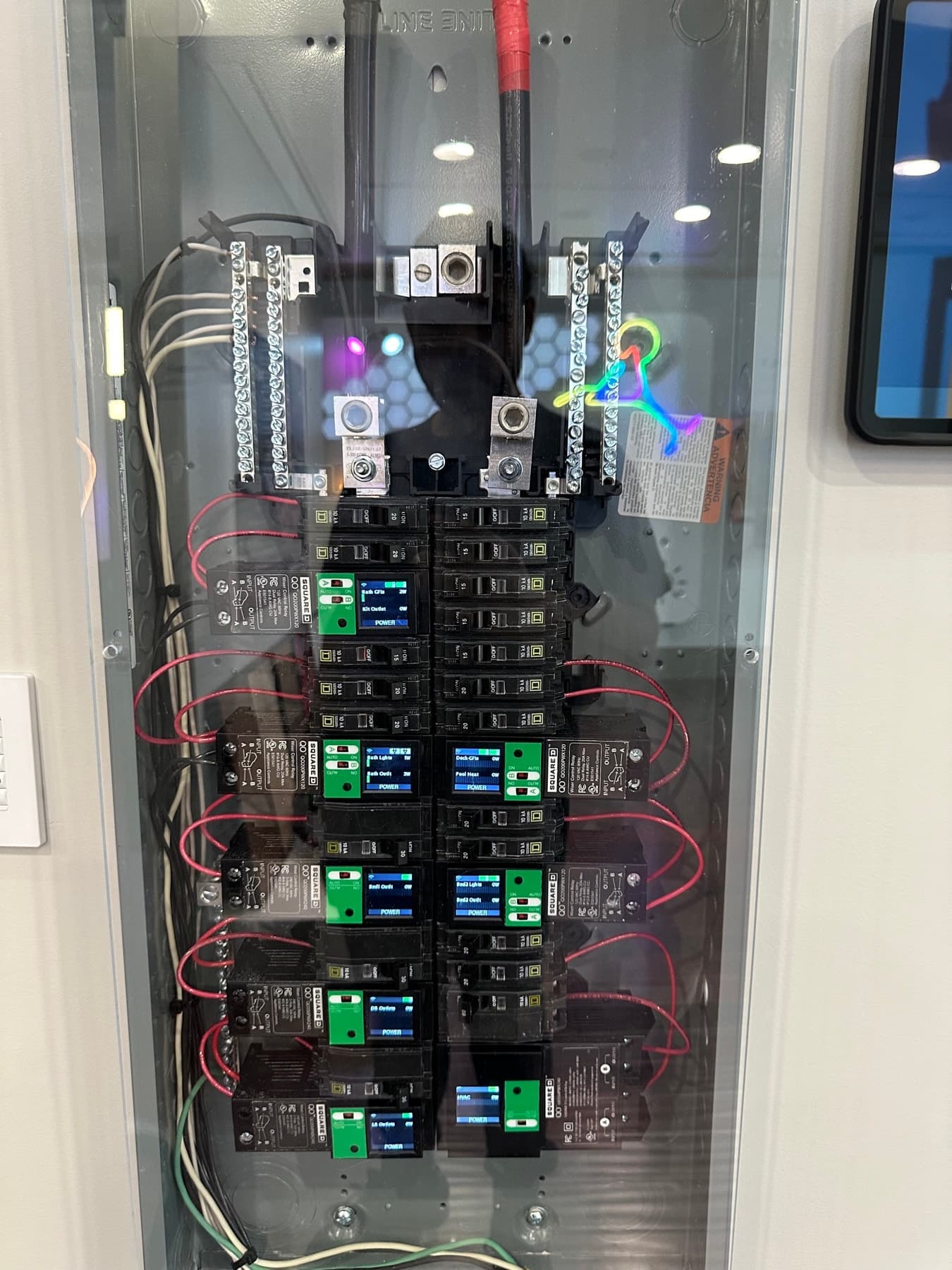 Smart electrical panel behind a clear cover: circuit breakers paired with load-control relay modules that show small status screens